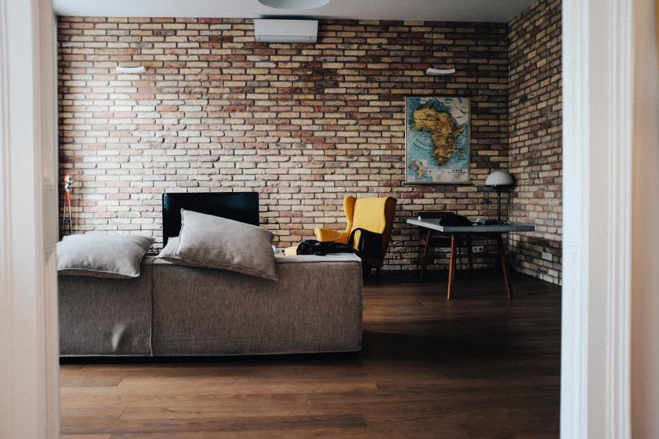 A low sectional sofa in front of a brick wall, with wooden floors and a desk in the background